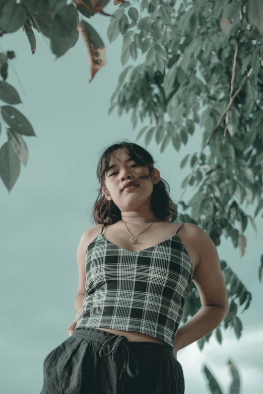 the young woman in a black and white checkered top stands in front of a tree