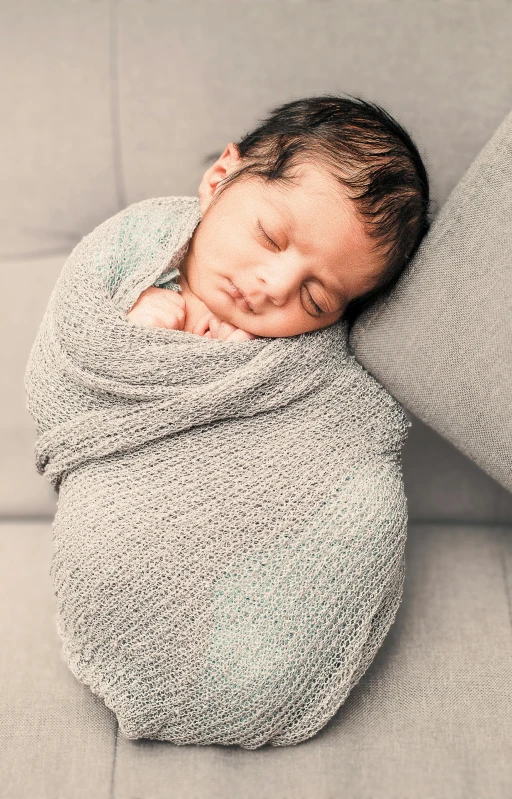 a newborn baby wrapped in a grey sweater is sleeping on a couch