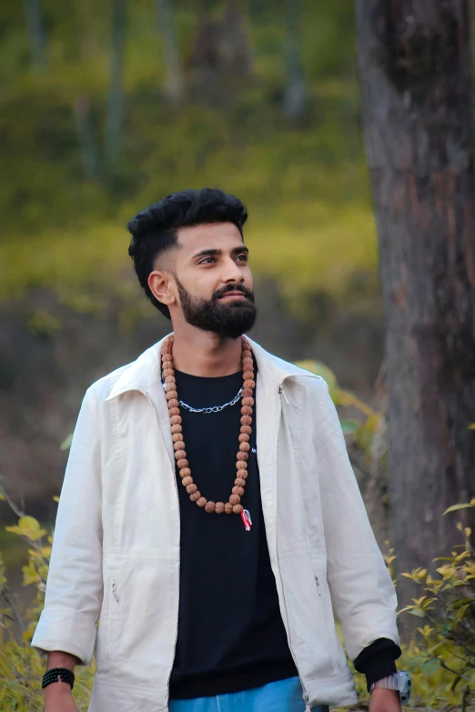 a man stands with a bead necklace in front of a tree