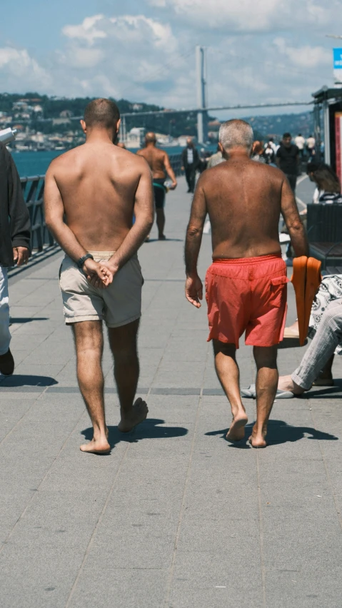 a group of shirtless men walk on the waterfront