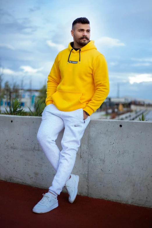 a man in yellow jacket leaning on wall next to brick plant