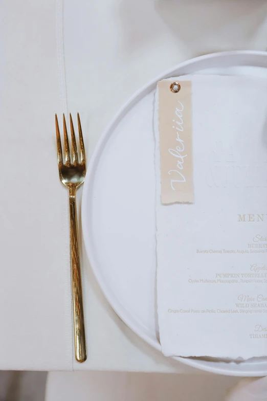 a white plate has a place setting with gold utensils and a fork