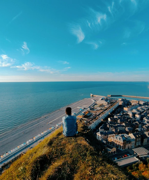 the man sits on the top of a hill looking out at the ocean