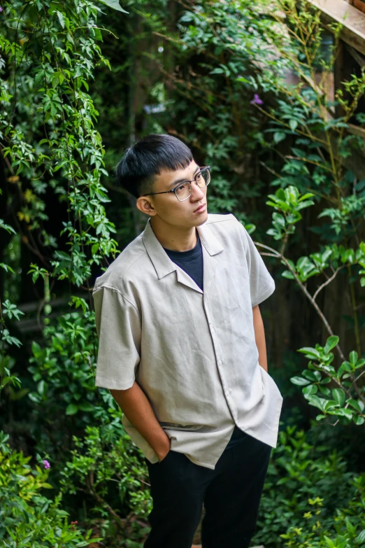 a man with glasses standing in front of trees and plants