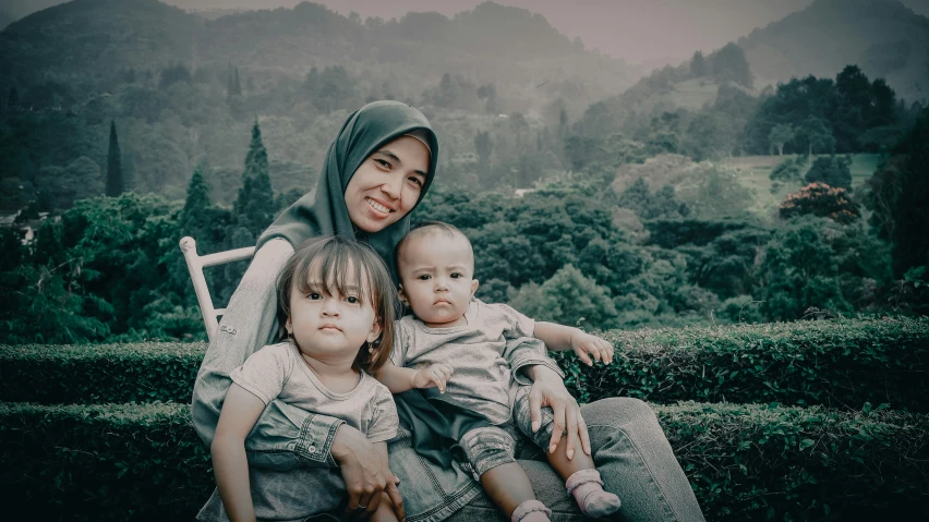 a lady with two children sitting on a bench in the middle of a garden