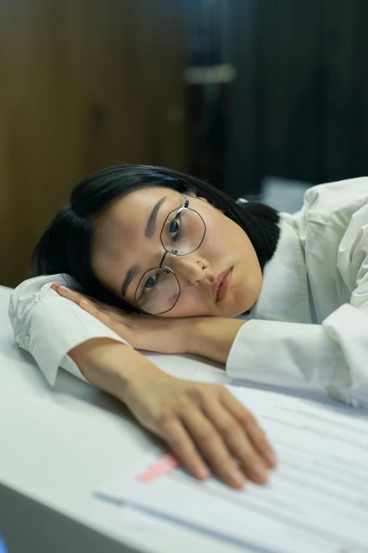 a woman leaning her head on a table next to papers