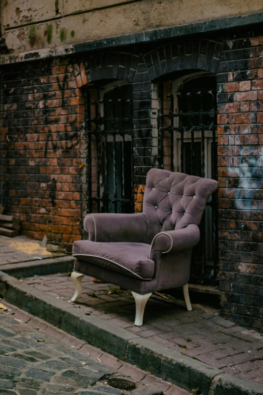 a purple chair sitting on a brick walkway in front of an old building