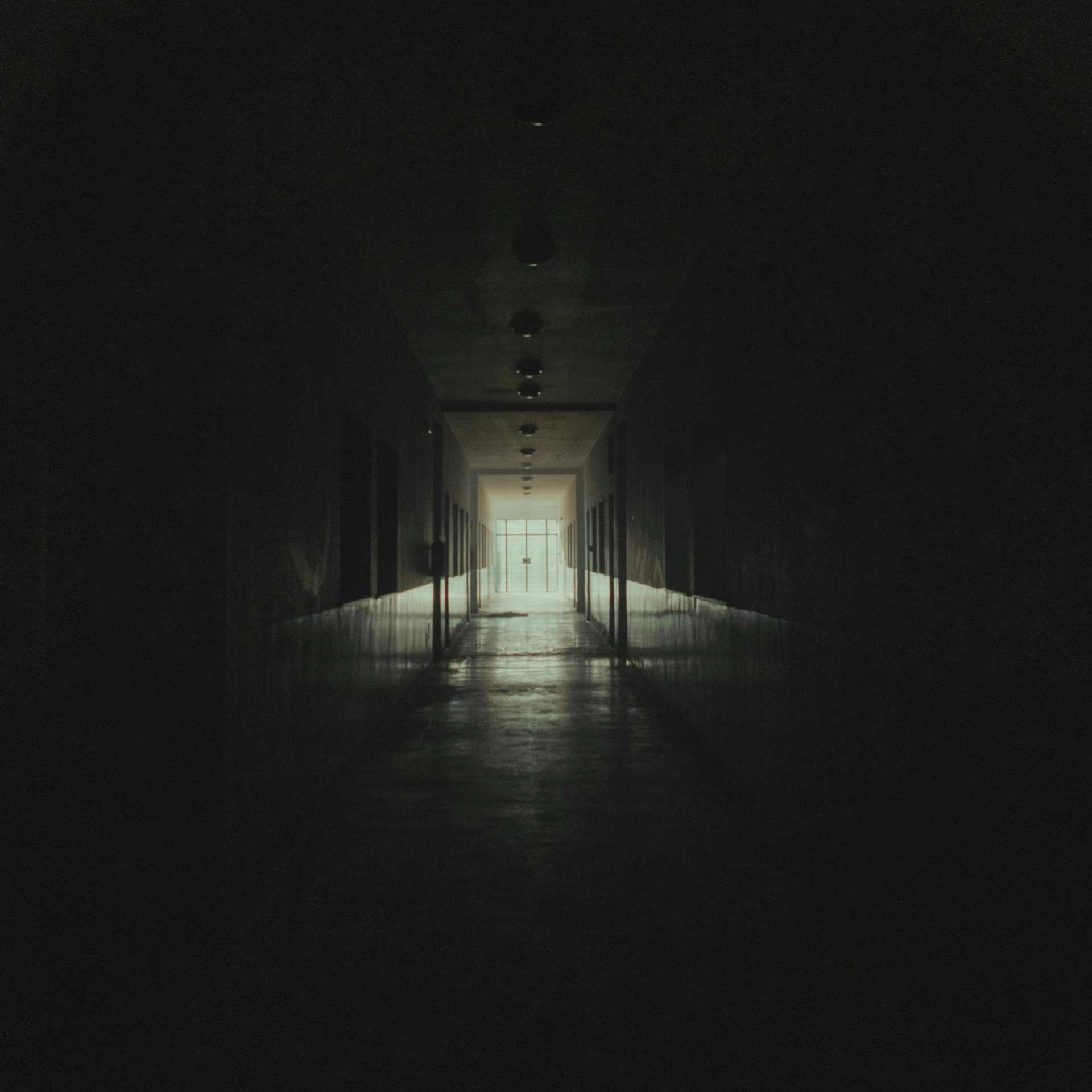 a dark hallway with light from the center and the door open