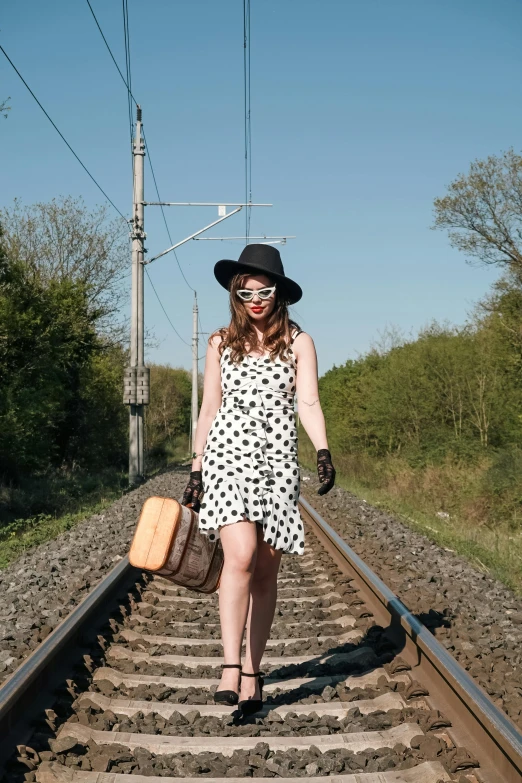 the lady is walking down the railroad track with a suitcase