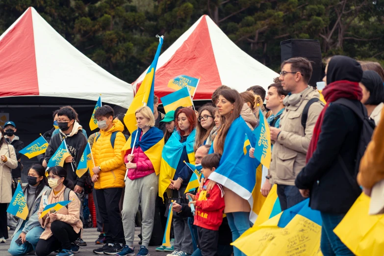 a crowd of people with flags and face masks standing in front of a group of large tents