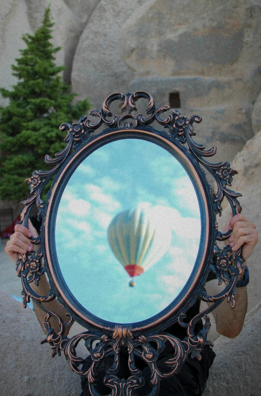 a hand holding up a circular painting with a  air balloon flying in the sky