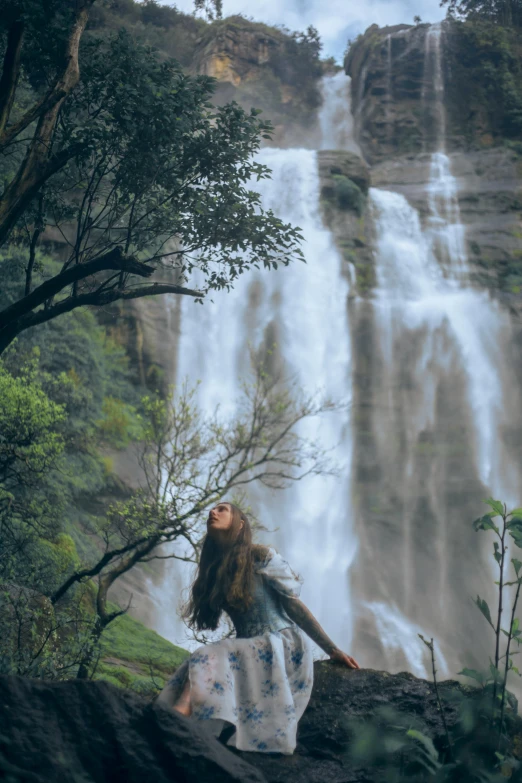 a woman is standing in the middle of trees looking at a waterfall