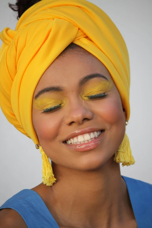 a smiling woman wearing a yellow head scarf and some yellow beads