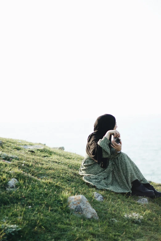 a woman is sitting on a hill looking out at the ocean