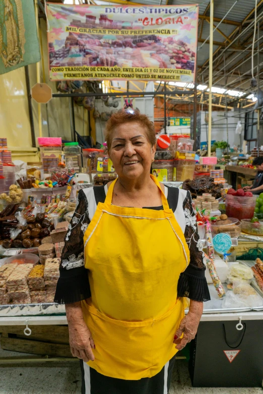 the woman wearing yellow apron is standing in front of a stall with food