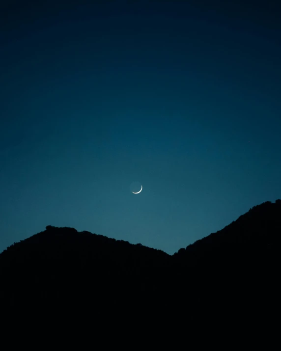 the moon is setting in the sky over the mountains