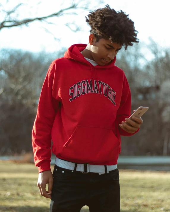 a young man stands outside looking at his phone