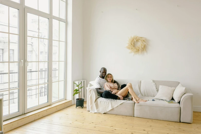 a man and woman sit on a couch in front of a window