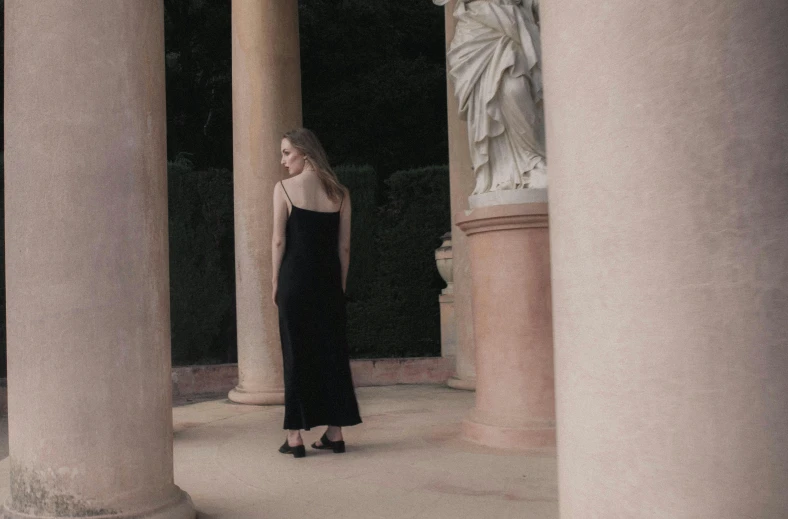 a woman wearing black and white is standing in a black gown surrounded by columns