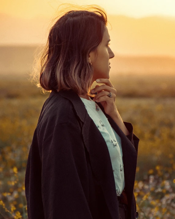 a woman standing in a field, with the sun low in the sky