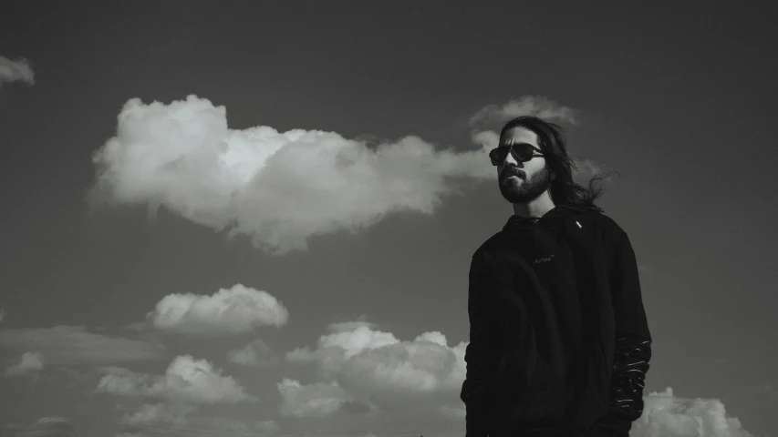 a man with sunglasses standing in front of clouds