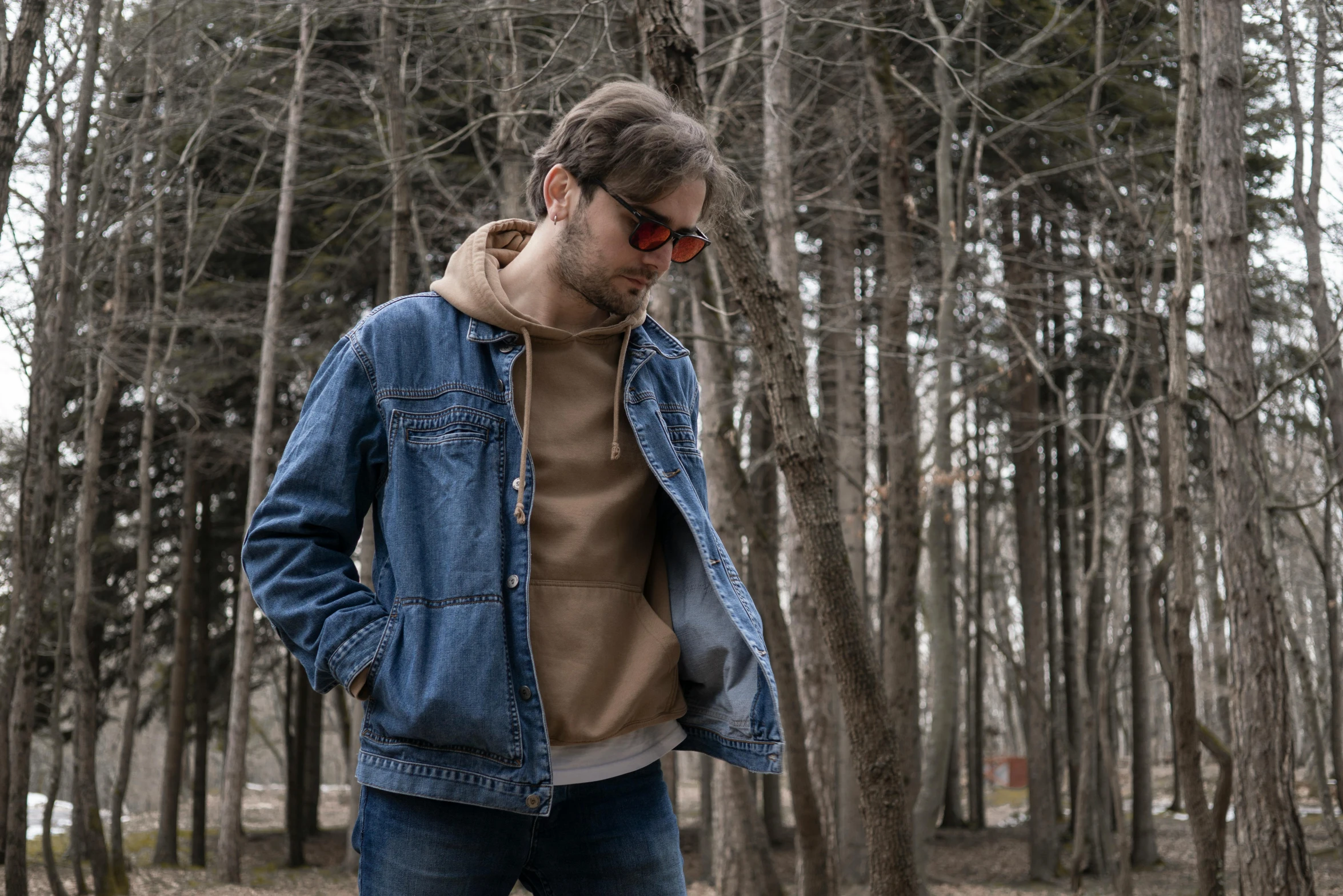 a man with glasses looking away and wearing a denim jacket