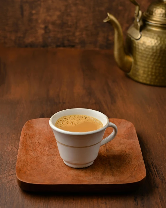 a cup of tea with a kettle of a liquid in the background