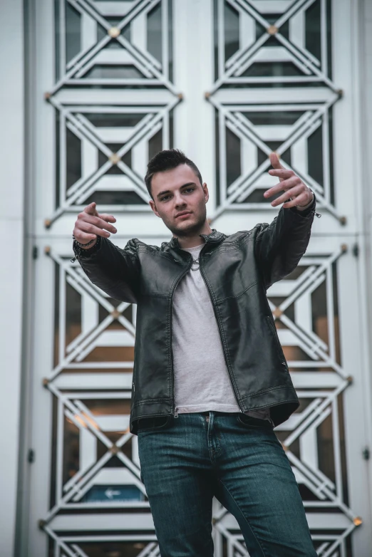 a man wearing a leather jacket is holding his hands out and standing on a bridge