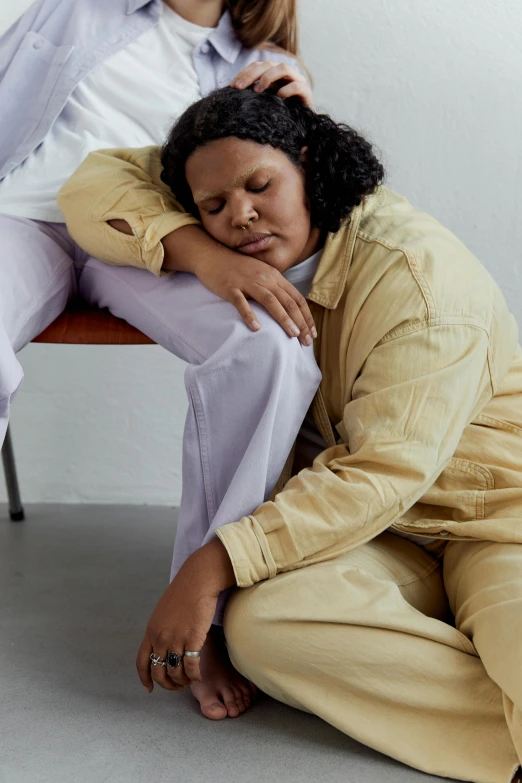 a woman in a white top is sitting on the floor with her arm around another woman's head and touching their hands to the top of her head