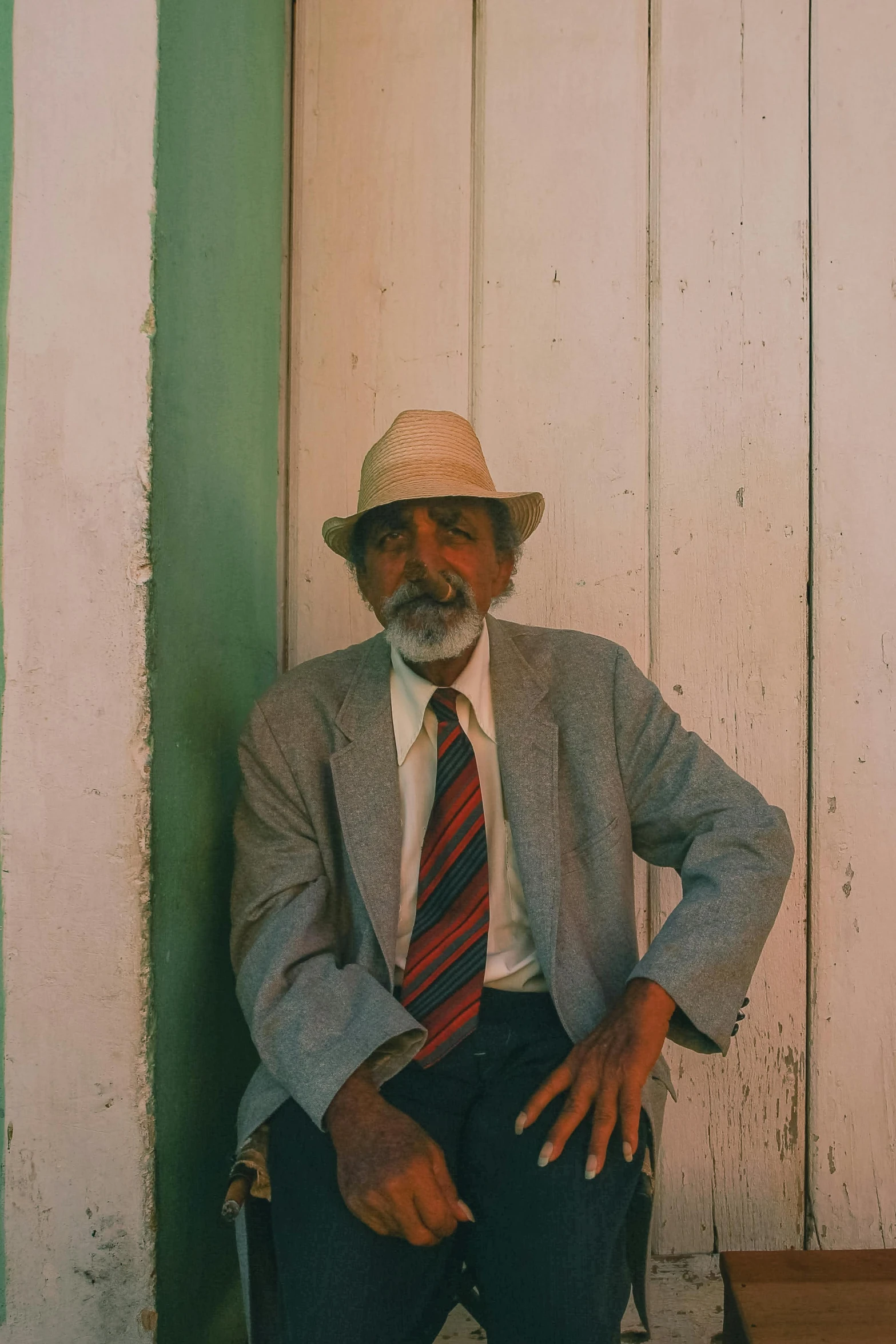 a man wearing a hat sitting down against a wall