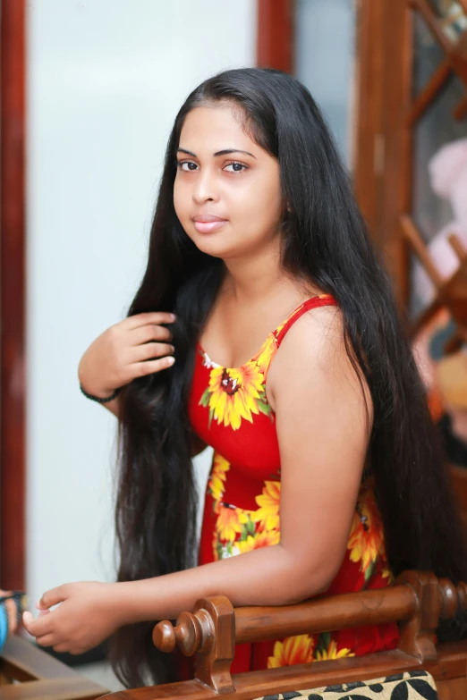 a woman in a yellow floral dress is leaning on a wooden chair and looking at the camera