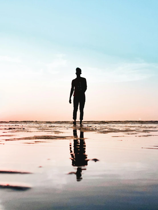 a person walking on a beach as the sun sets