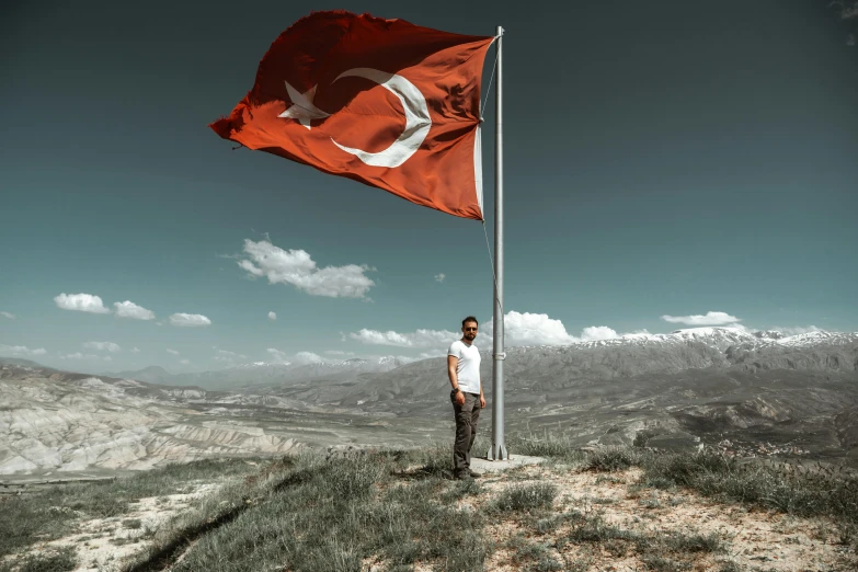 a man standing in front of a large flag on a hill