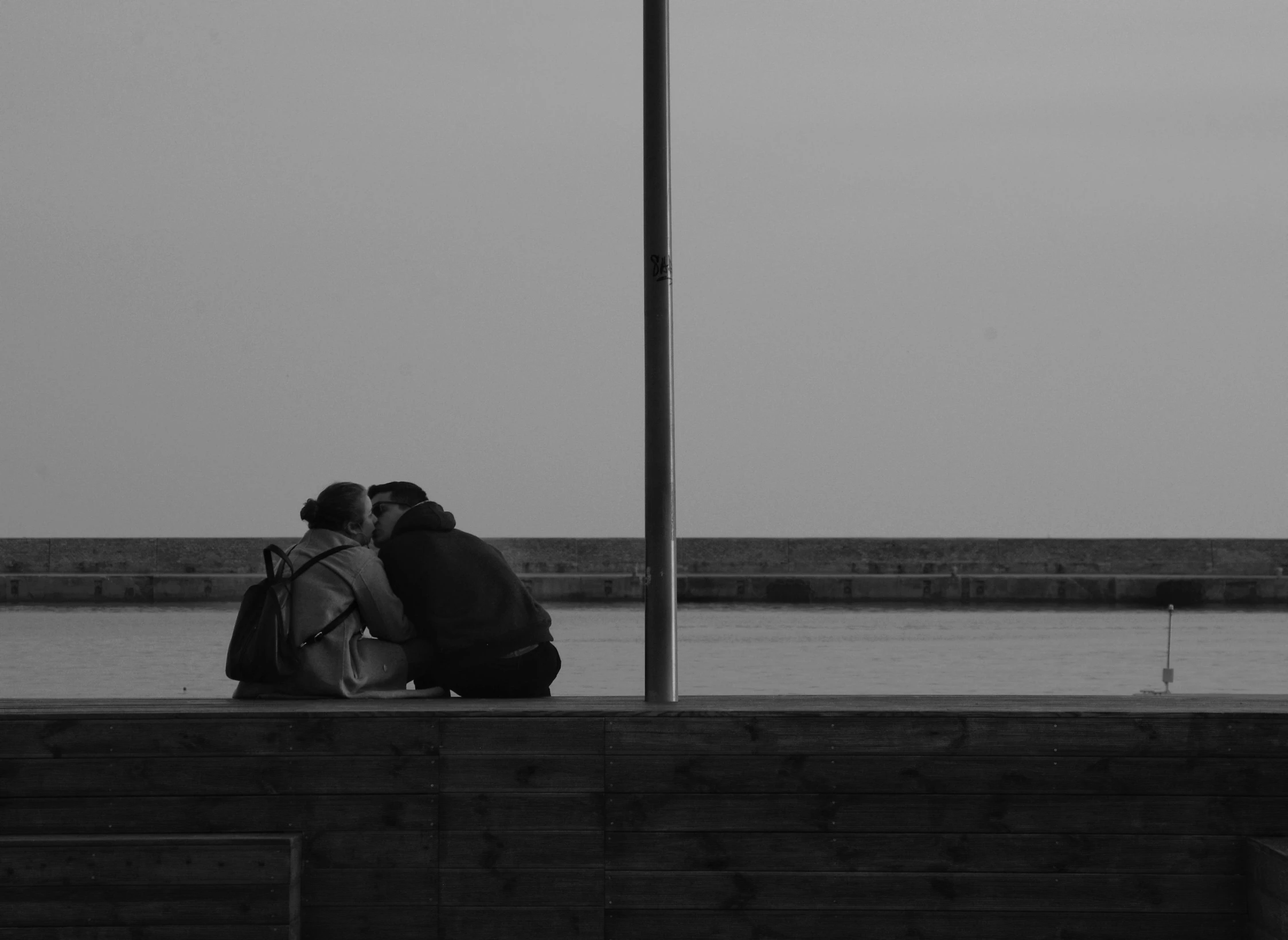 two people sitting on the top of a wall near the water