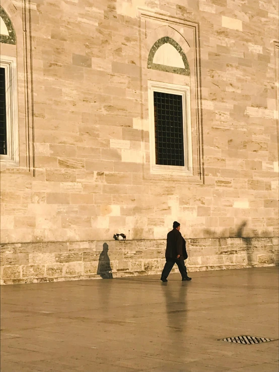 the man is walking down the sidewalk near some windows