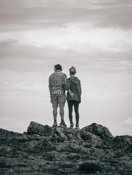 two people looking out at the sky from a rocky summit