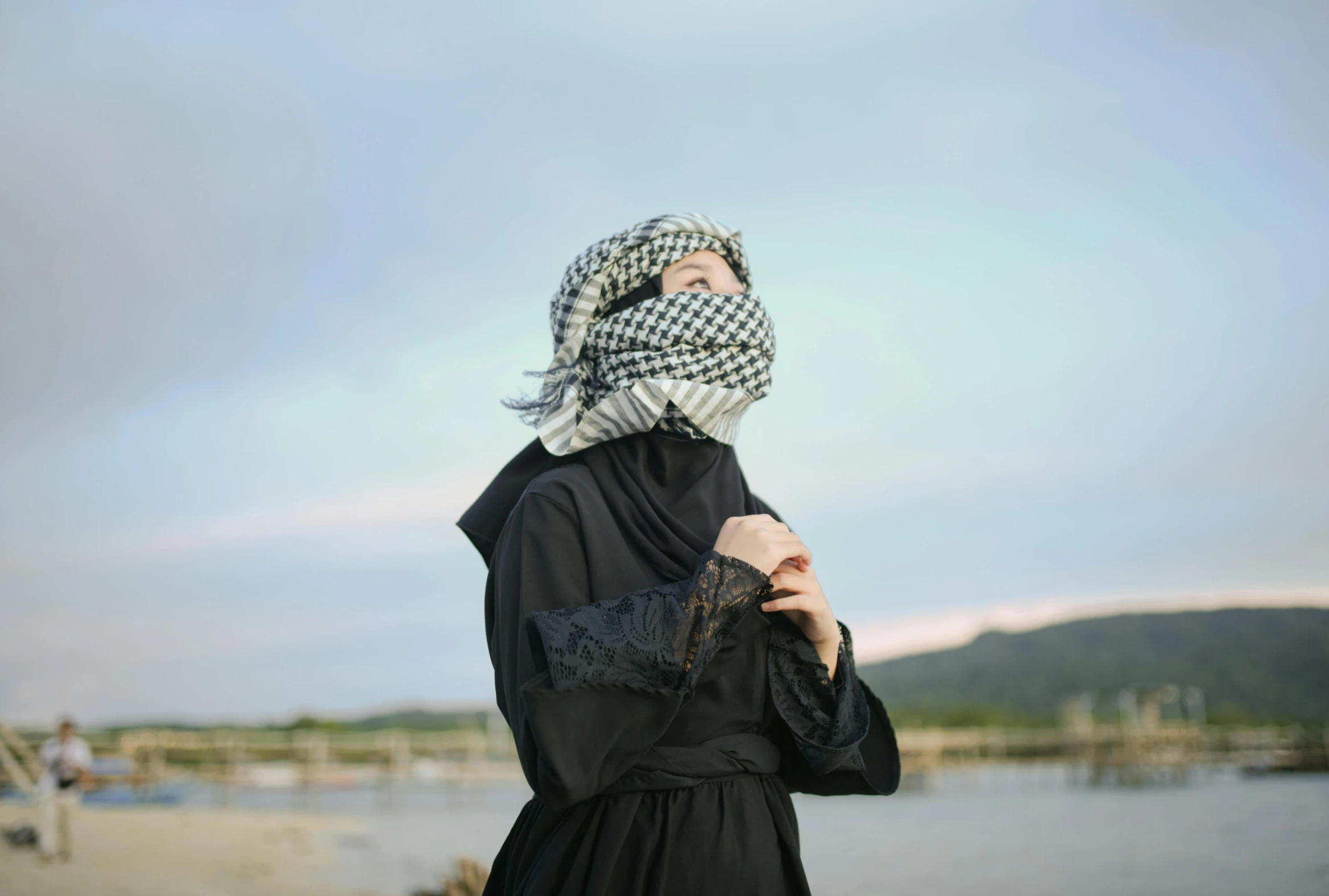 a woman in a black dress and headscarf by a lake