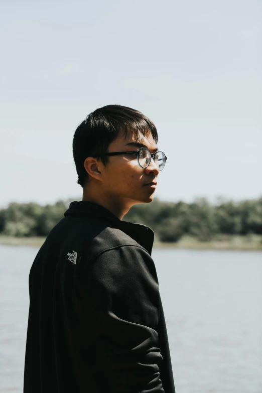 a young man in glasses stands near the water