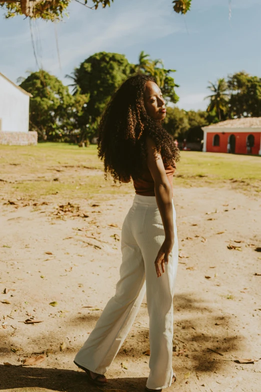 woman with afro wearing white pants, looking off to her right