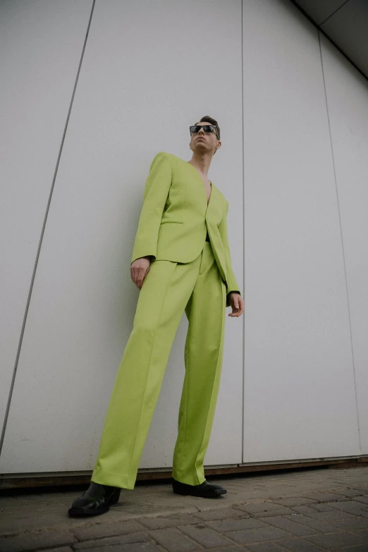 a man in a green suit leaning against a wall