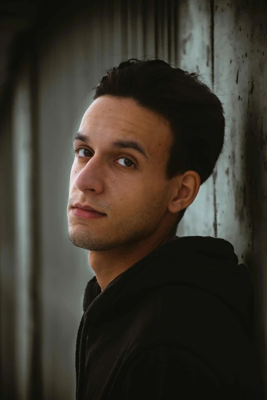 a man poses for a picture while against a wall