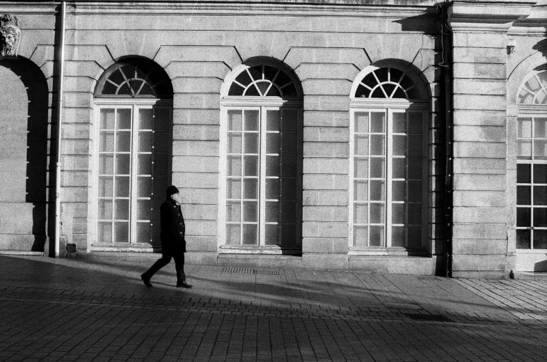 a man walking past a large building with tall windows