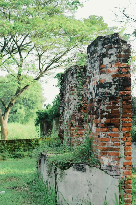 the side of a brick structure sitting in a grass field next to a tree