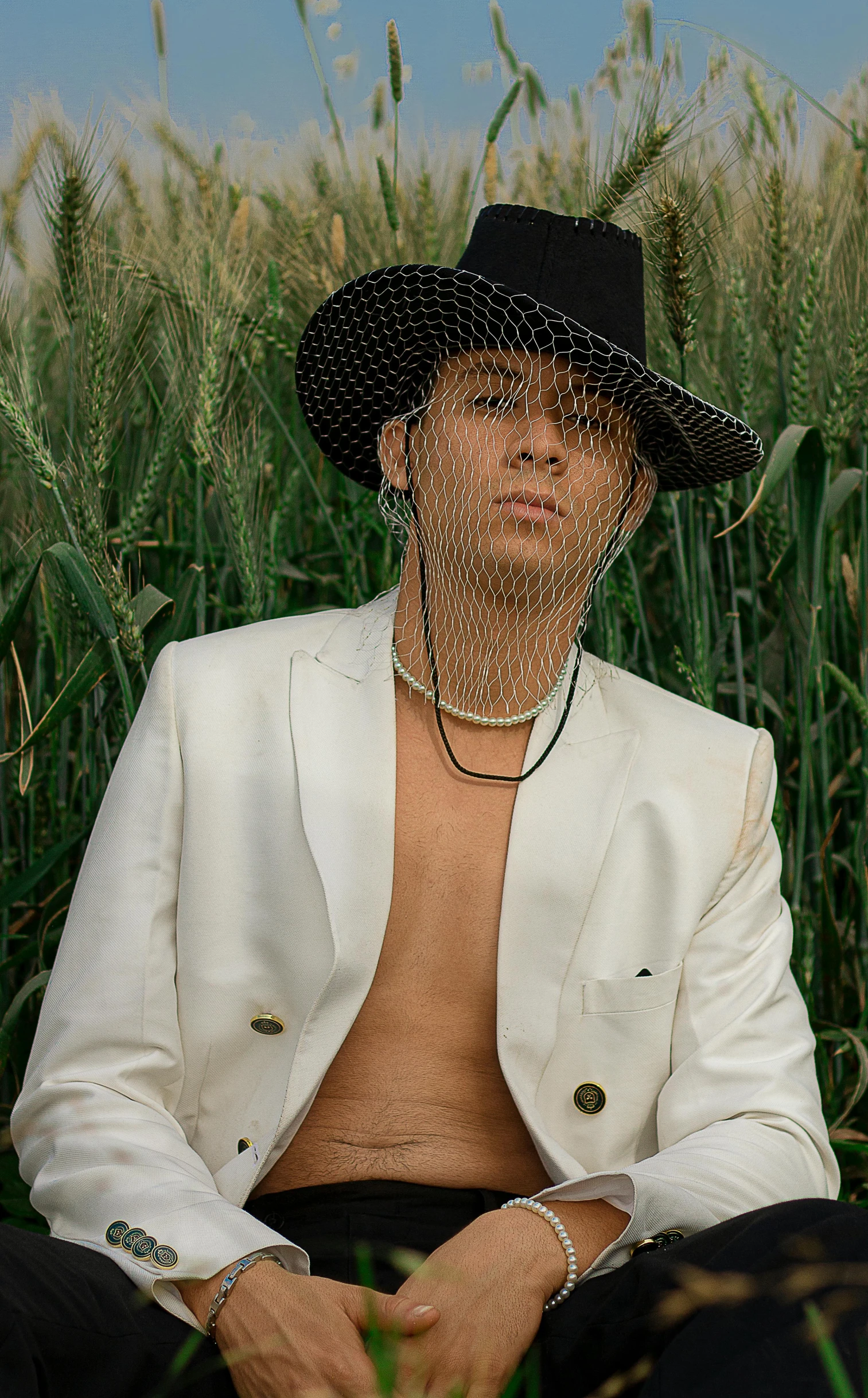 a shirtless man sitting in tall grass wearing a hat