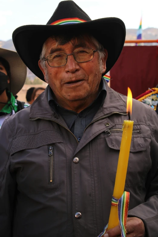 a man in black hat holding a candle with a yellow stem