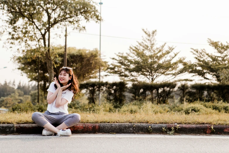 a woman in striped pants sitting on the curb on her phone