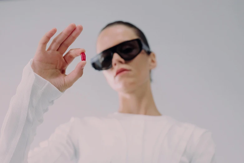 a woman wearing shades is holding out a red pills in front of her