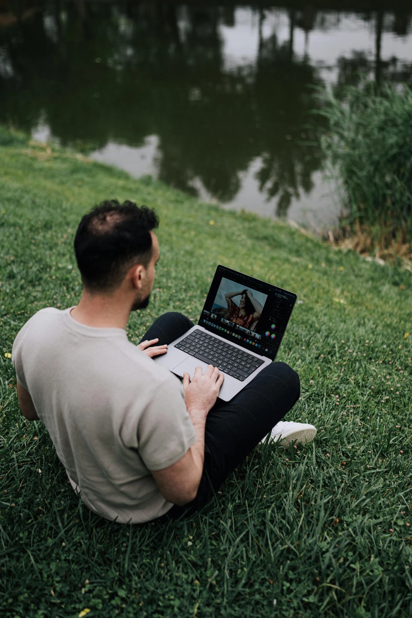 a man is sitting on the grass, working on his laptop