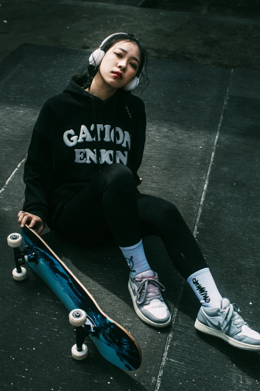 a girl sitting on the pavement with headphones sitting on a skateboard