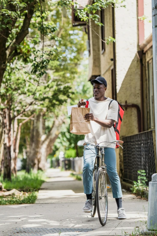 man in white shirt on bicycle holding up a bag